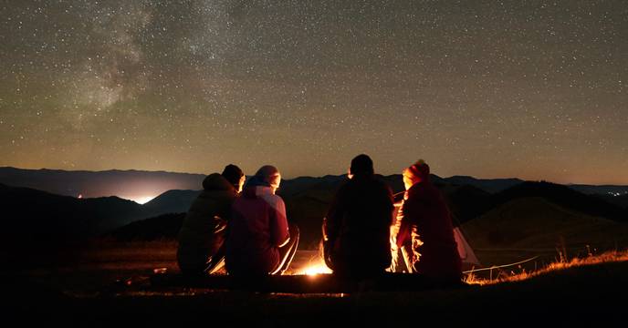 Group of people under the starry sky around the campfire