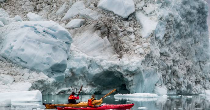 Two people in a kayak with an icy landmass as a backdrop