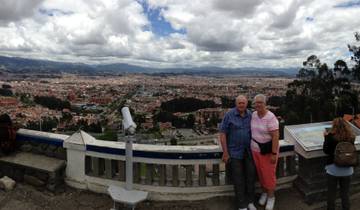 Two older adults posing at a viewpoint overlooking a large city.