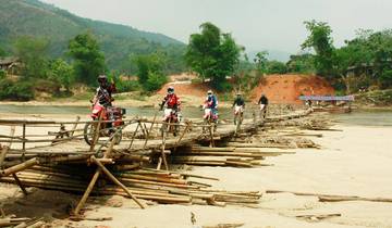 Riders crossing a bamboo bridge in a rural area.