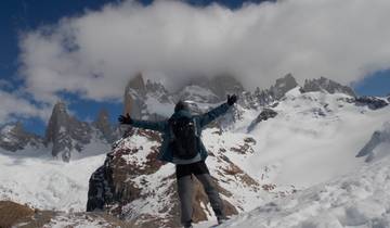 Person joyfully reaching out towards towering snowy peaks.