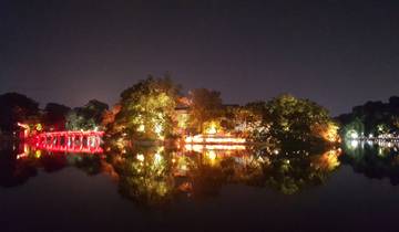 Bridge and trees illuminated with bright lights reflecting in water at night.