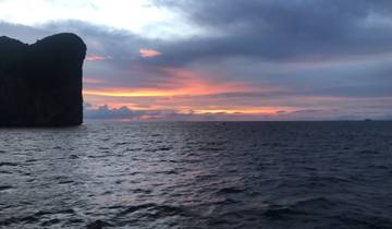 Ocean at sunset with dramatic sky and cliff silhouette.