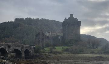 Stone castle with a stone bridge and hills in the background.