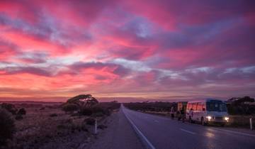 A vibrant sunset over an open road, with a bus parked on the side.