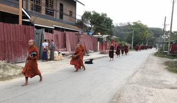 Monks walking in a line down a street with red fences.
