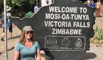 Woman sitting in front of a welcome sign for Victoria Falls.