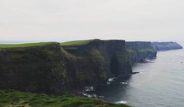 Majestic cliffs overlooking the ocean, partially cloudy sky.