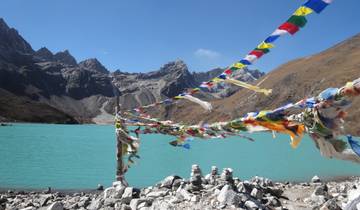 Colorful prayer flags hanging over a turquoise lake with mountains in the background.