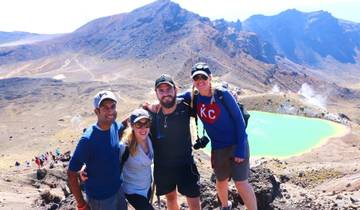 Four people in hiking gear posing on a mountain with a turquoise lake in the background.