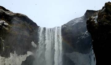 Waterfall cascading down a cliff with a rainbow on the right side.