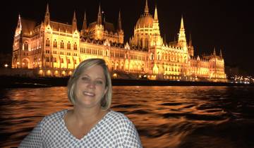 Woman smiling with the illuminated Hungarian Parliament Building at night.