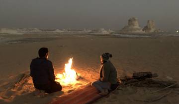 Two people sitting by a campfire in the desert at dusk.