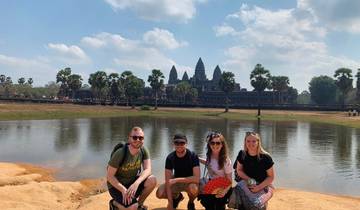 Four people posing in front of Angkor Wat with a lake.