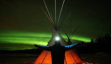 Silhouette of a person in front of a tipi with the Northern Lights in the background.