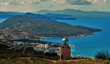 A coastal town with a lighthouse and sprawling mountain scenery.