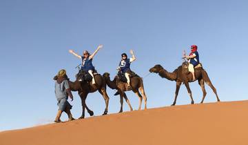 People riding camels on sand dunes with a guide.