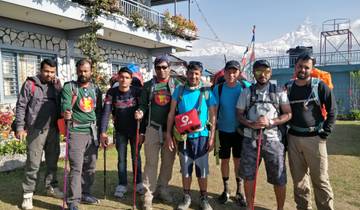 Group of hikers posing in front of a building with mountains.