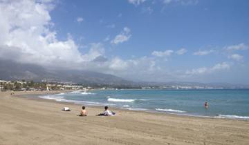 People relaxing on a sandy beach with mountains in the background.