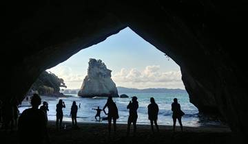 Silhouettes of people in a cave entrance with a beach view.
