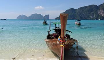 Traditional longtail boat anchored on a clear blue sea with distant islands.