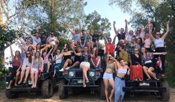 Large group of people posing on jeeps in a forest setting.