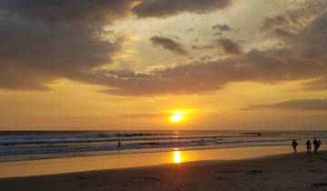 A beach during sunset with people walking by the shore.