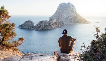 Person sitting on a cliff overlooking the ocean and rocky islands.