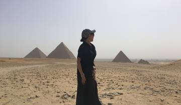 Person standing in front of pyramids in the desert.