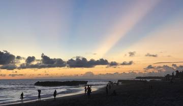 A beach scene during sunset with silhouettes of people.