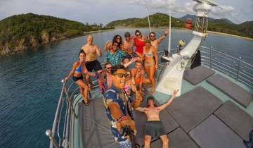 Group on a boat posing for a selfie with a coastal background.
