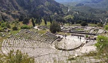 Ancient stone amphitheater surrounded by trees and mountains.