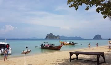 Boats docked by a sandy beach with distant rocky islands.