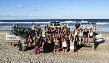 A large group of people posing with vehicles on a beach.