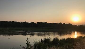 Sunset over a river with silhouettes of distant trees.