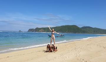 Three people forming a human pyramid on a sandy beach with a boat in the background.