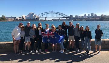 A group of people with an Australian flag in front of a harbor with iconic landmarks.