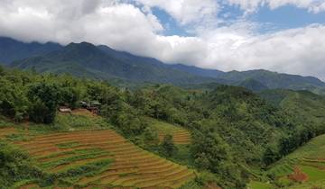 Terraced rice fields in a mountainous landscape under a partly cloudy sky.
