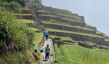 People walking along terraced ruins on a hillside.
