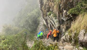 Group of hikers on a narrow trail on a misty mountainside.