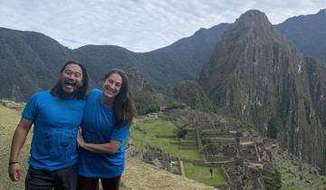 Two people smiling with mountains and ancient ruins in the background.