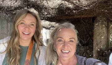 Two smiling women under a vine-covered canopy.