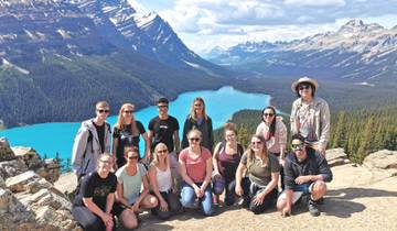 Group posing on a cliff with a breathtaking view of a turquoise lake and mountains.