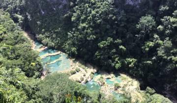 Aerial view of terraced turquoise pools in a forest.