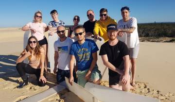 Group photo of people posing with surfboards on a sandy beach.