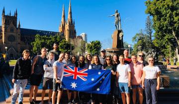 Group of people holding an Australian flag with a historical building in the background.