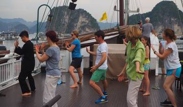 Group on a boat exercising or dancing with scenic cliffs in the background.