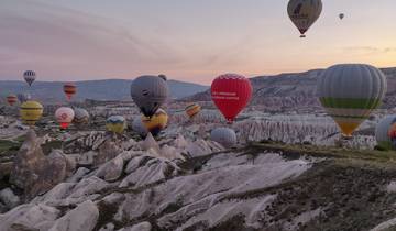 Hot air balloons in the sky over a rocky Cappadocian landscape.