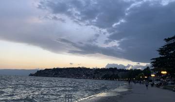 A waterfront promenade during twilight with street lamps and distant hills.