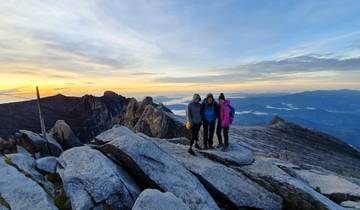 Three people posing on a rocky mountain peak at sunrise.